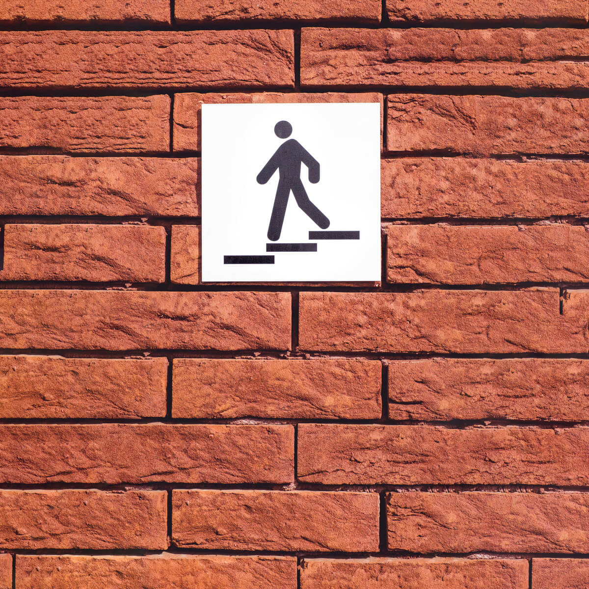 Imagen del exterior de una oficina con una placa de acero inoxidable rotulada con el pictograma de un monigote bajando las escaleras.