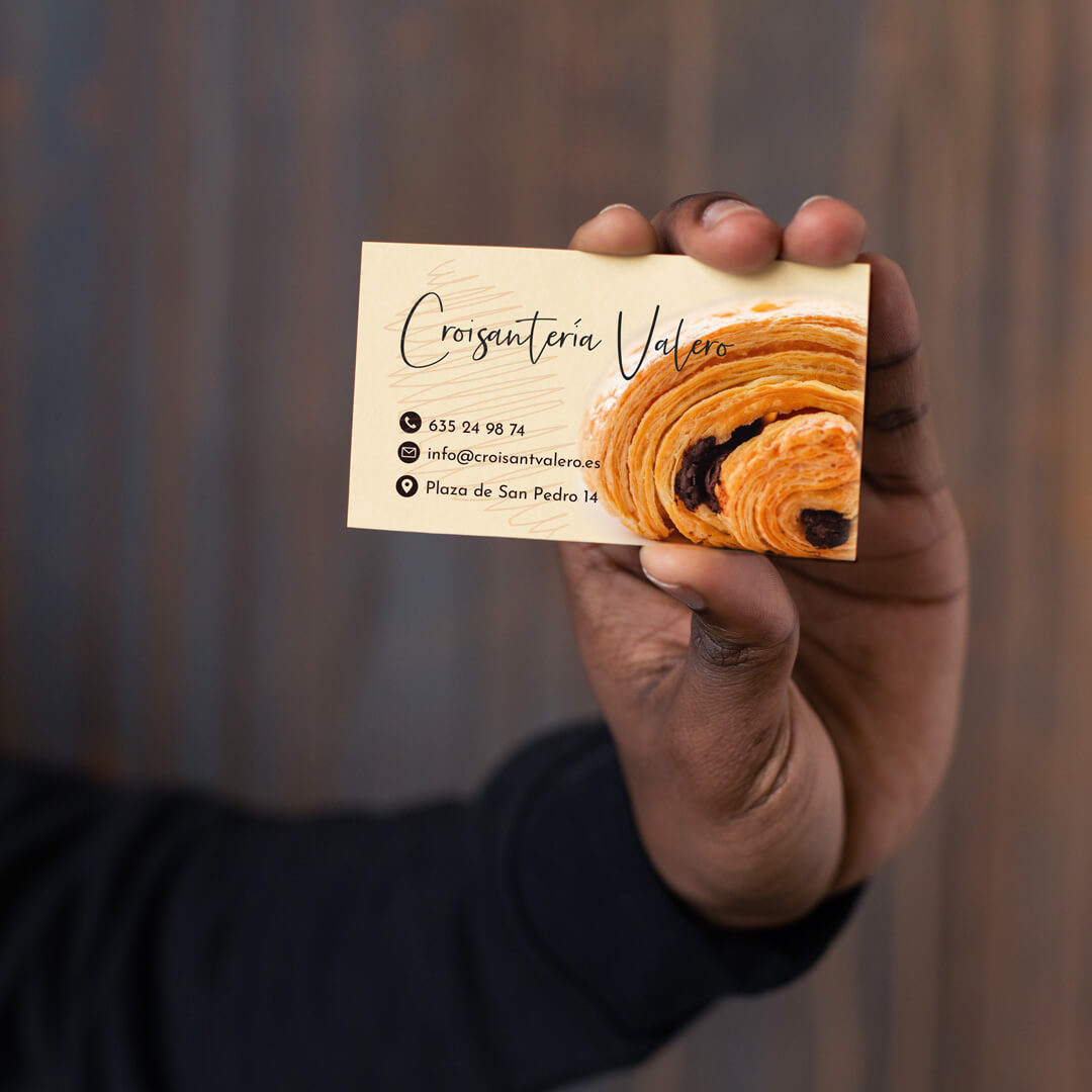 Imagen de una persona sosteniendo la tarjeta de visita de la croissantería valero, conde aparece el logotipo de la marca, un croissant y la información de contacto de la emrpesa.