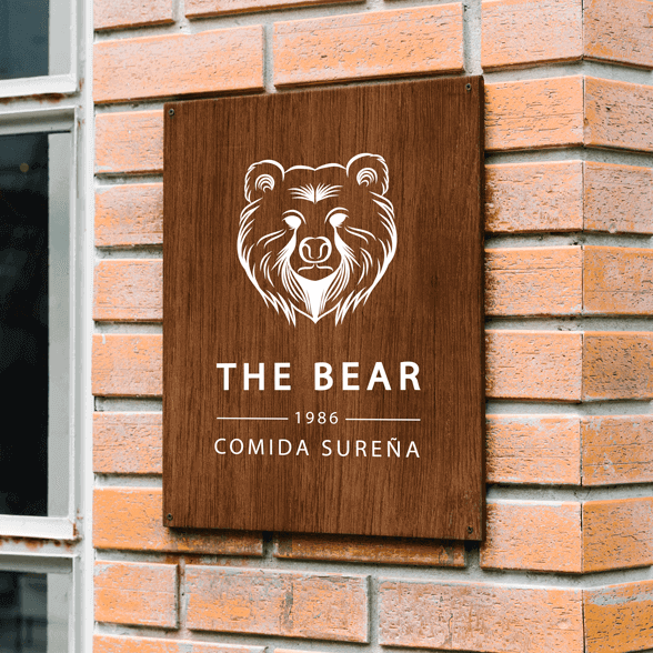 Imagen de un letrero de madera donde se ha impreso directamente el logotipo del restaurante "The Bear". El letrero está expuesto en la fachada exterior del restaurante.