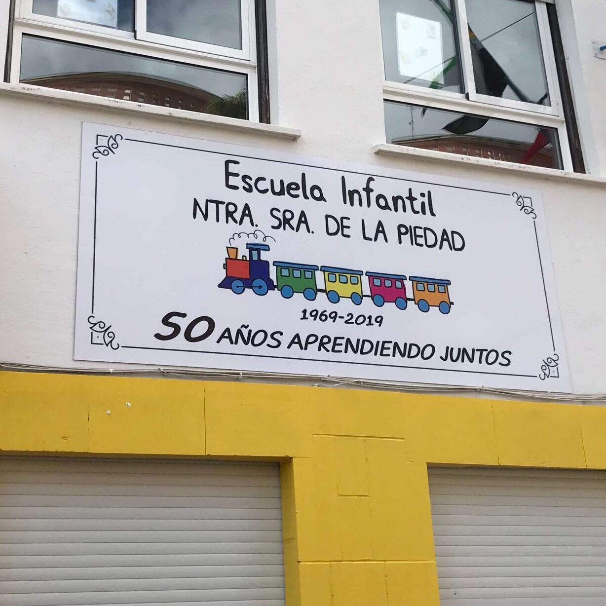 Imagen del letrero de la Escuela Infantil Nuestra señora de la piedad, rotulado en chapa y colocado sobre la fachada del edificio.